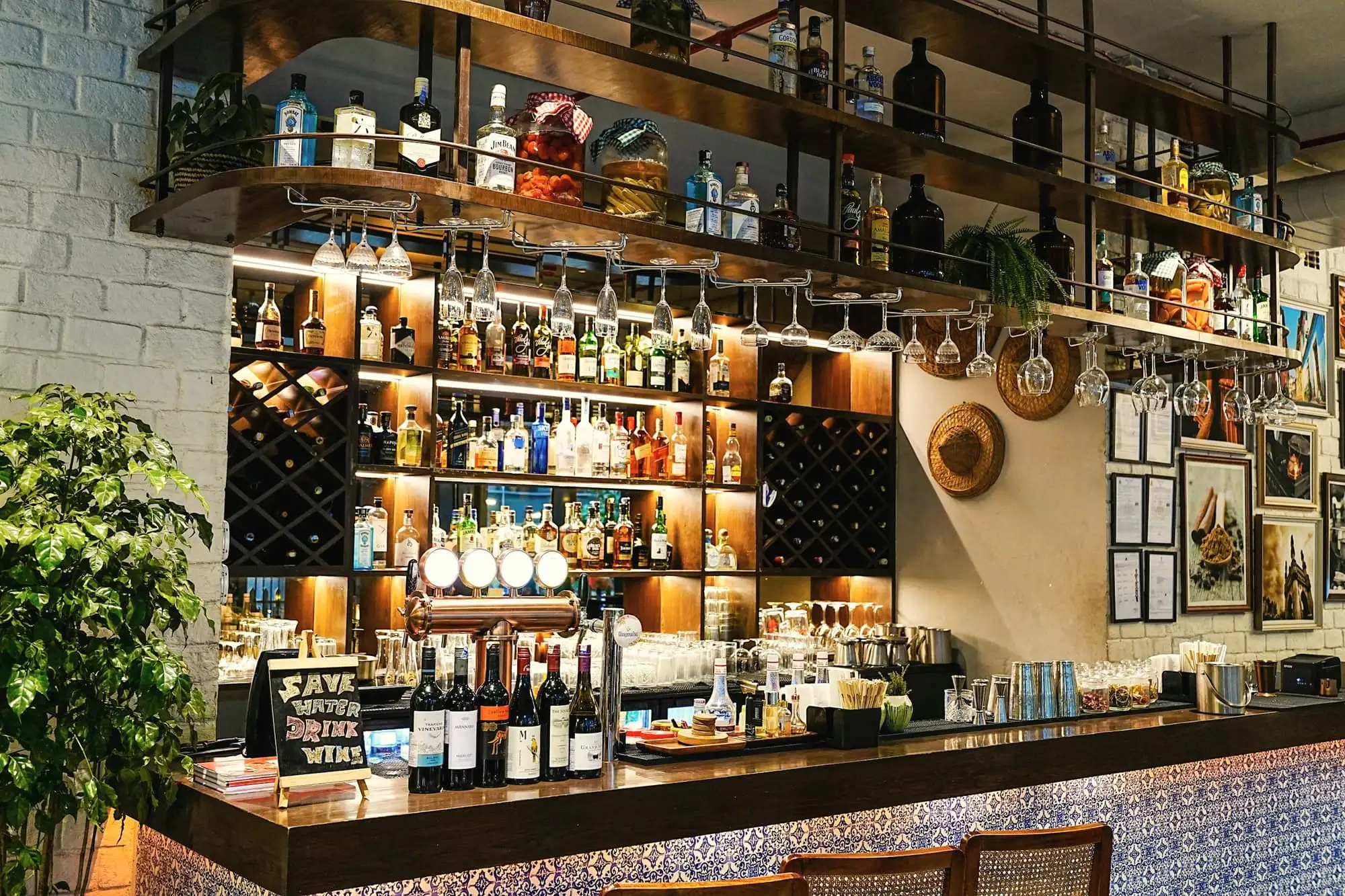 A bar counter faced with blue and white tiles, with shelves of bottles and hanging glasses behind it.