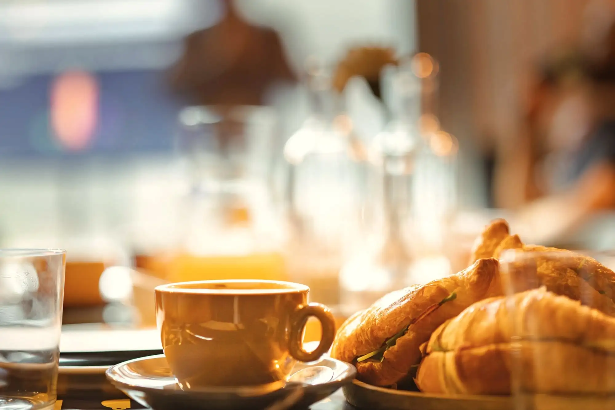 A cup of coffee and two croissants on a small table, in warm, soft light.
