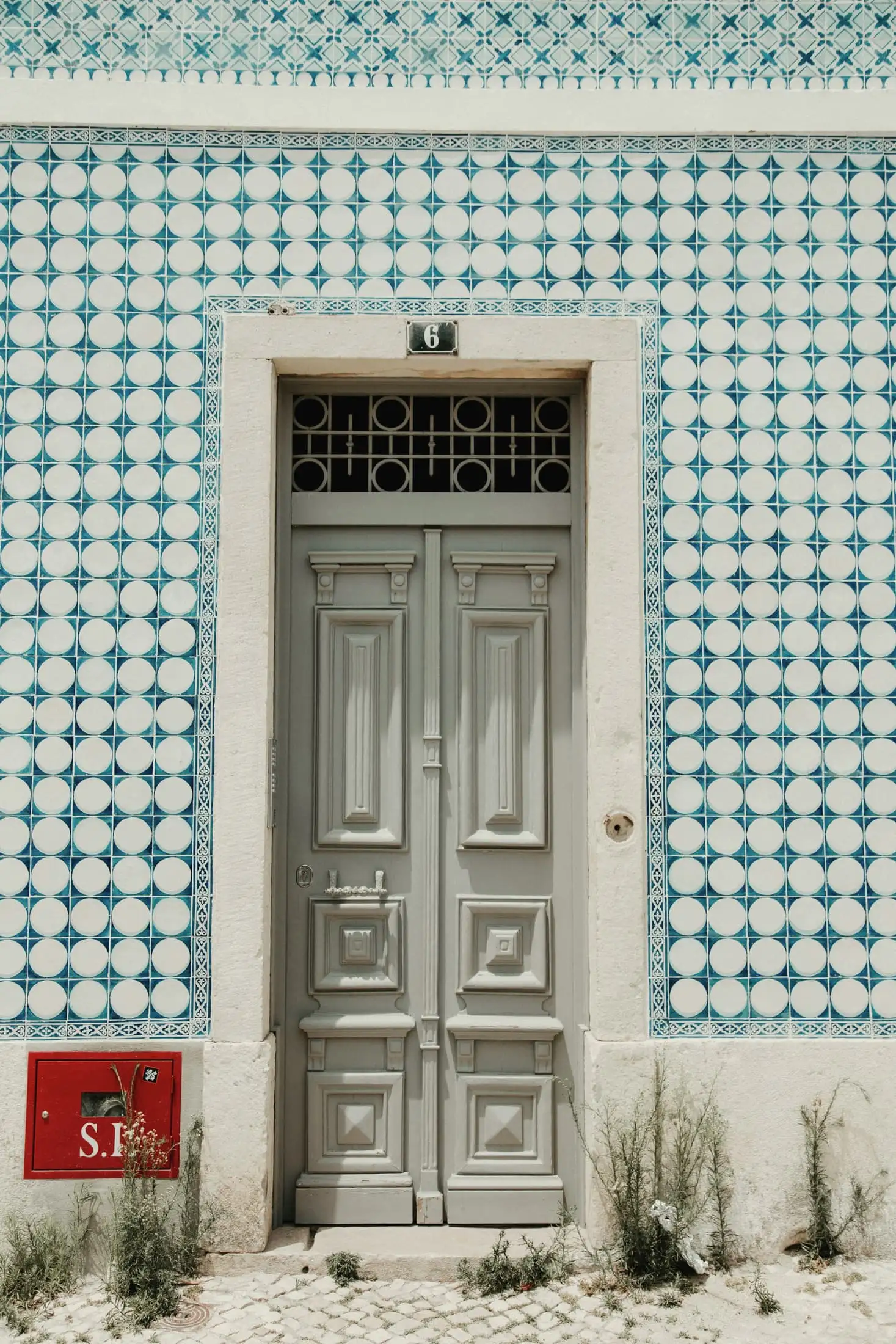 A tall grey double door in a wall of green and white diamond-patterned tiles, with a small house number above it.