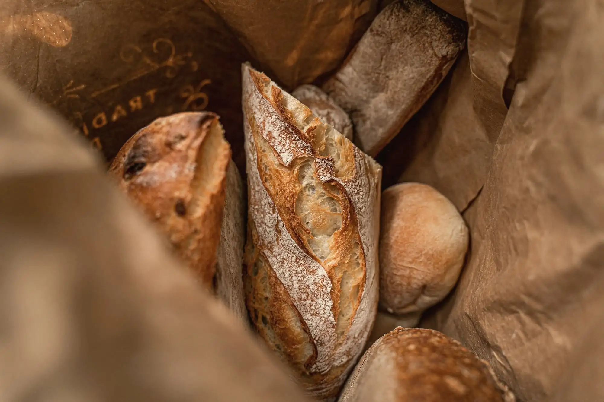 Crusty loaves and rolls in a brown paper bag on a wooden counter.