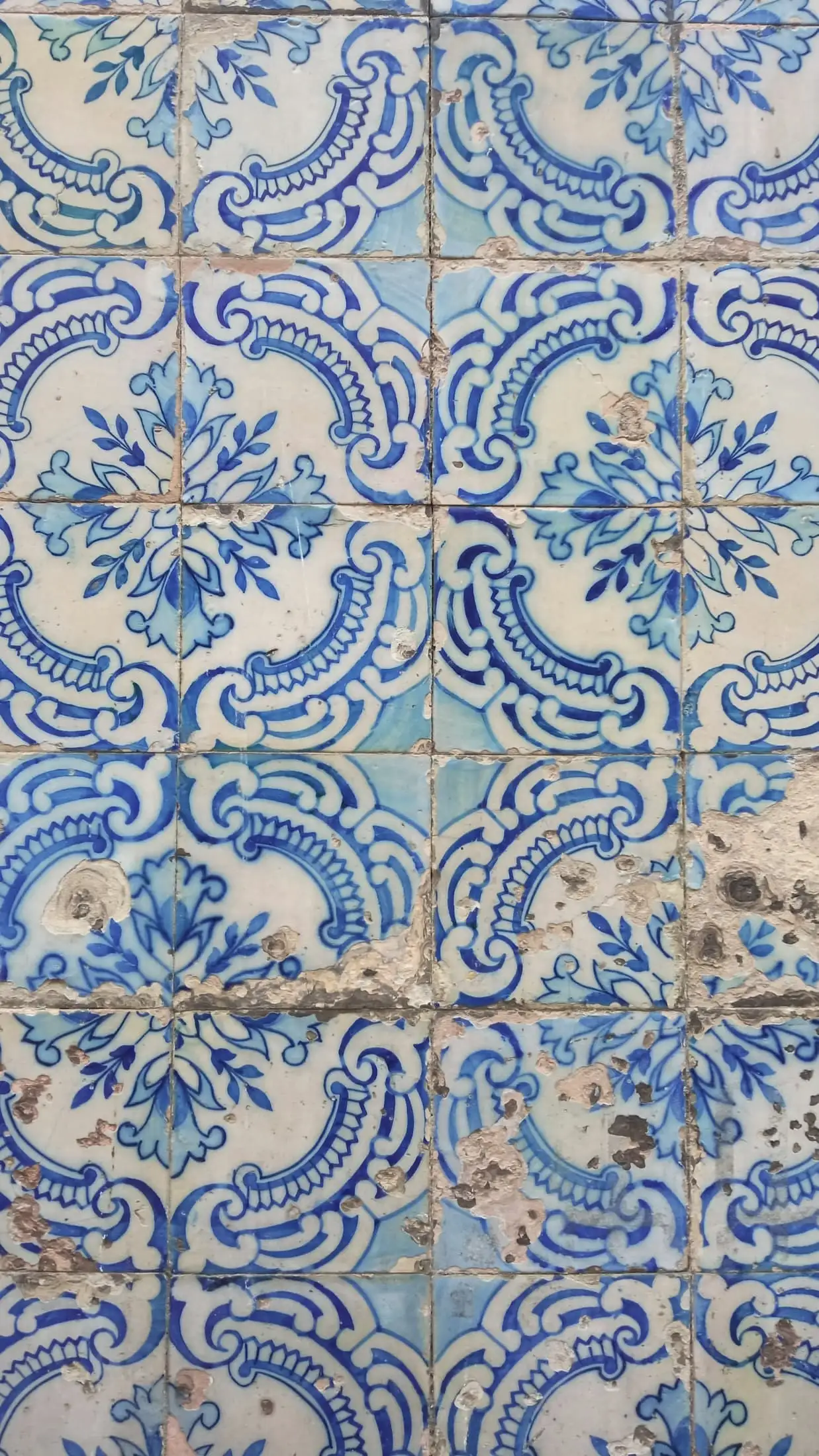 A wall of blue and white glazed tiles with a repeating floral pattern and some chipped edges.