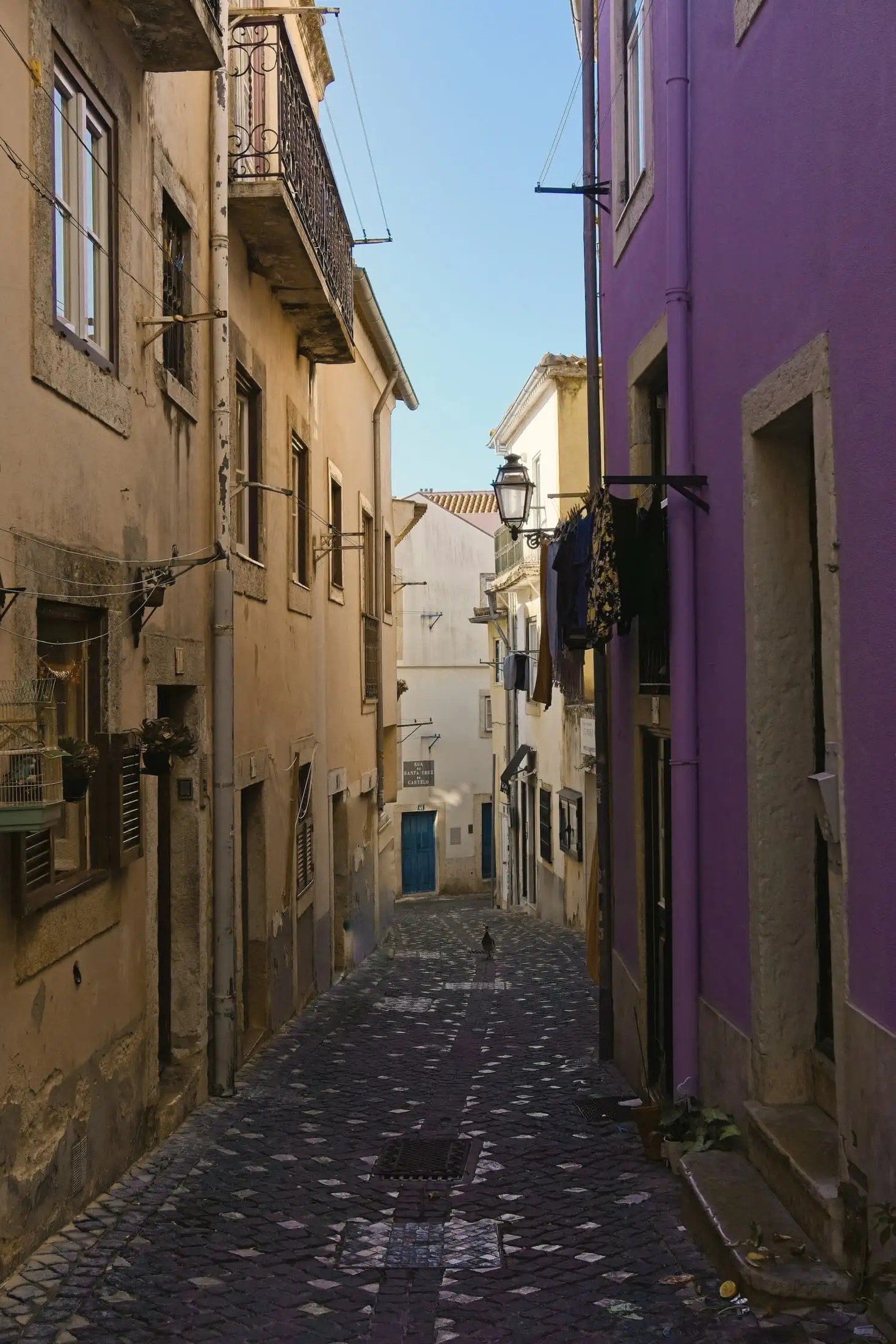 A narrow cobbled lane between ochre and purple houses, with washing hung from a window and a lantern on the wall.
