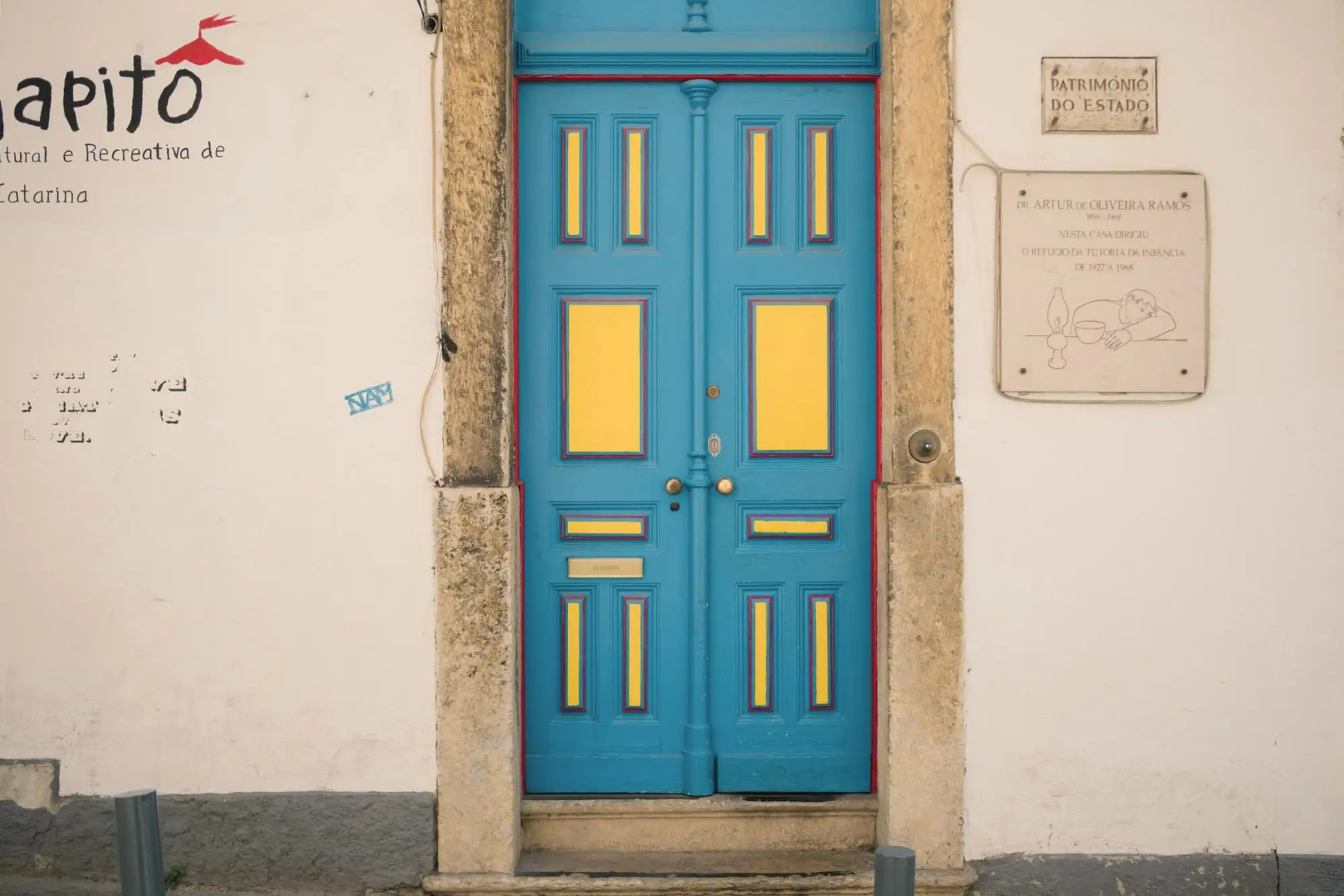 A blue double door with yellow panels set in a white wall beside a stone plaque.