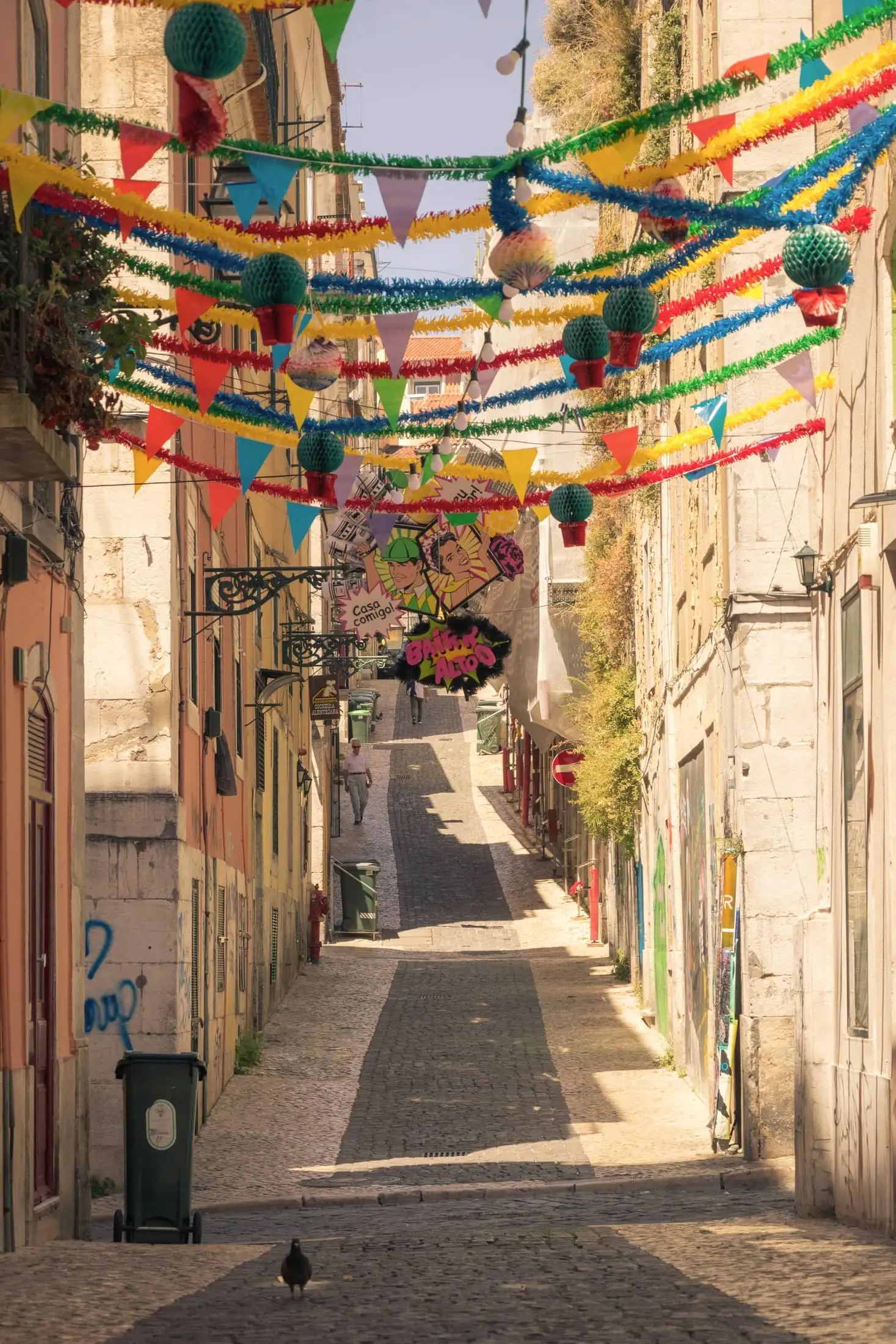 A narrow lane strung with coloured paper bunting, between pink and cream houses with iron lamp brackets.