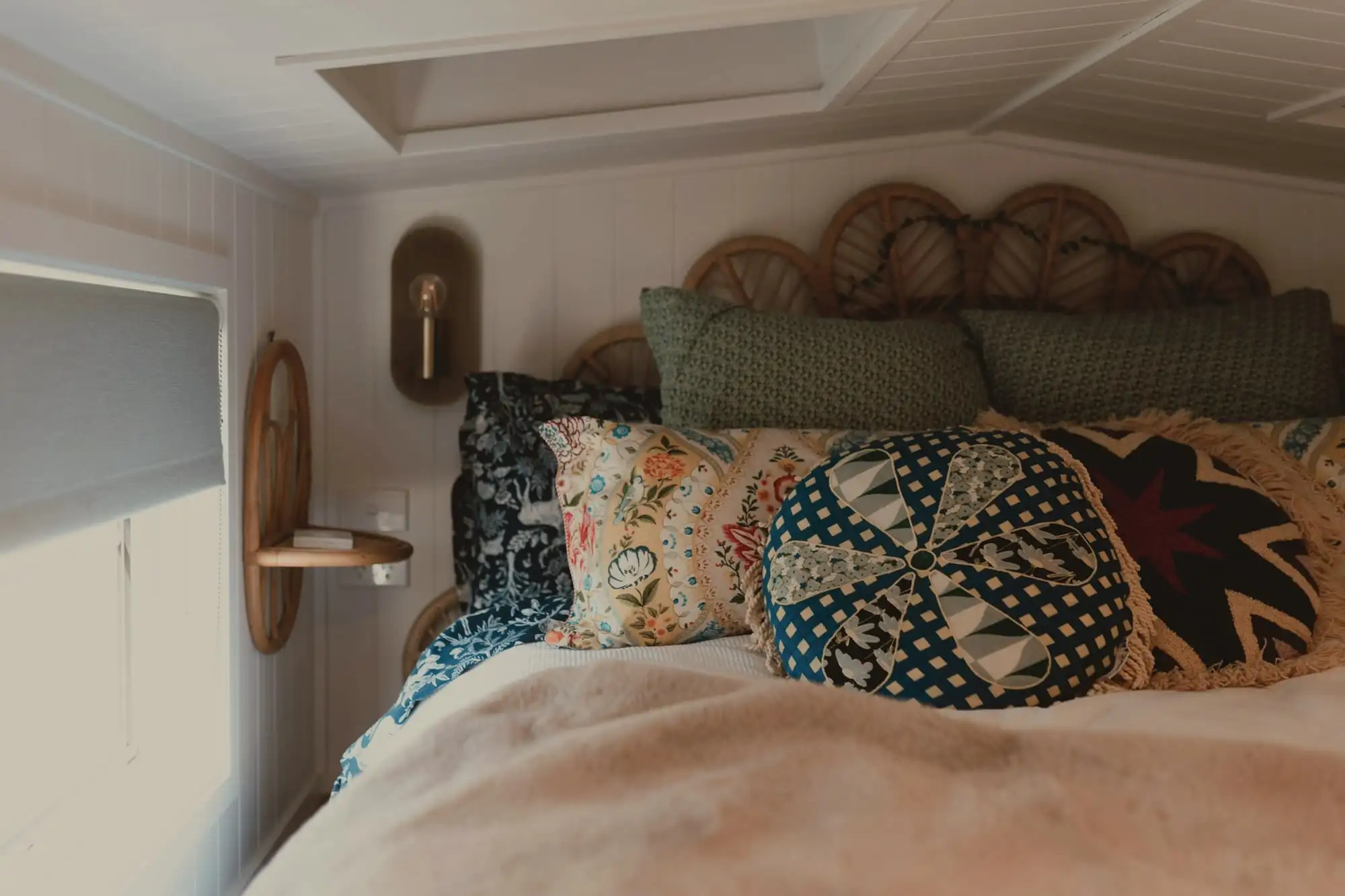 A bed with patterned cushions under a wicker headboard, in a small attic room with a skylight.