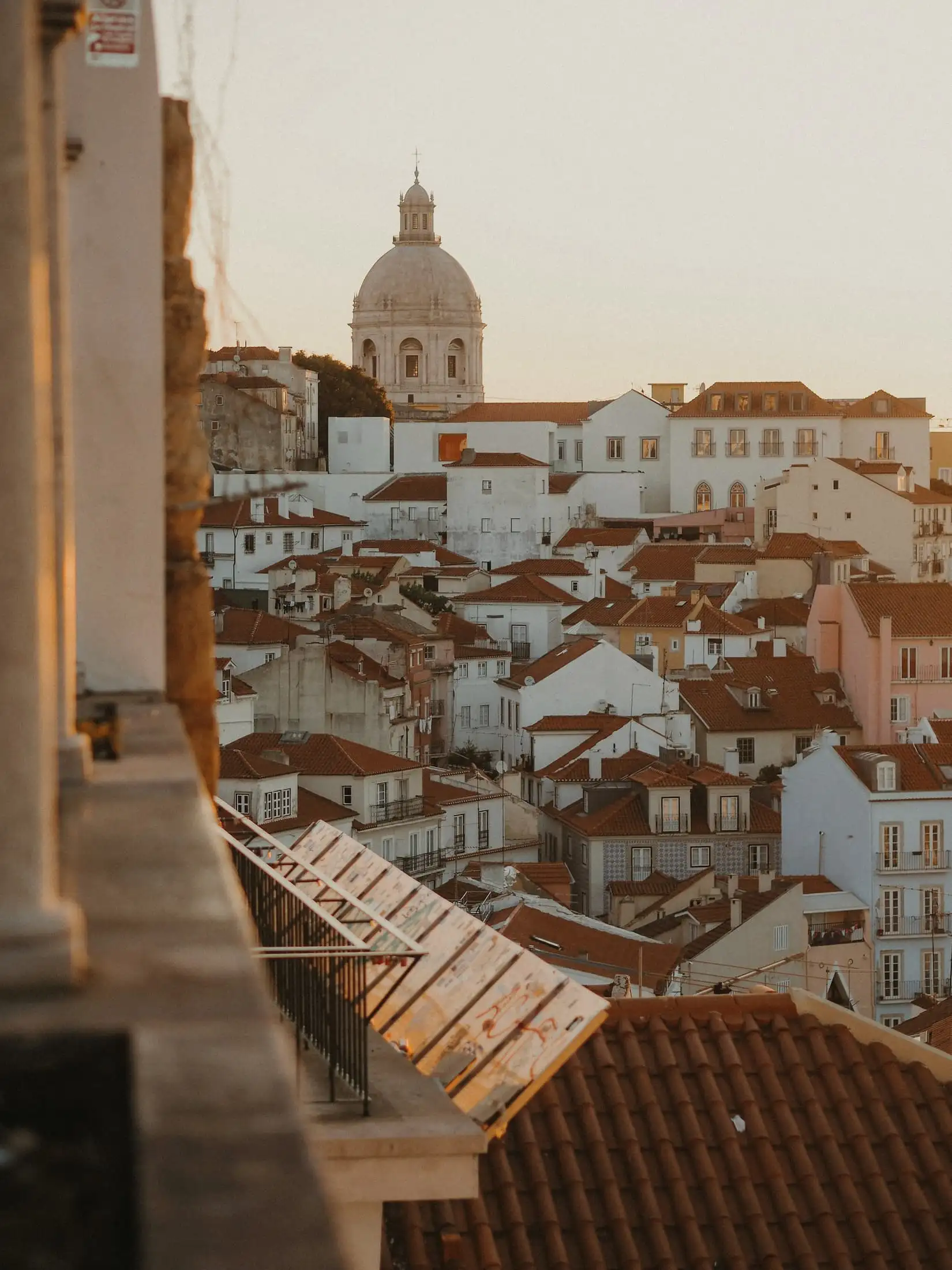 Terracotta roofs and a white church dome lit gold by low sun, seen from a stone balcony.