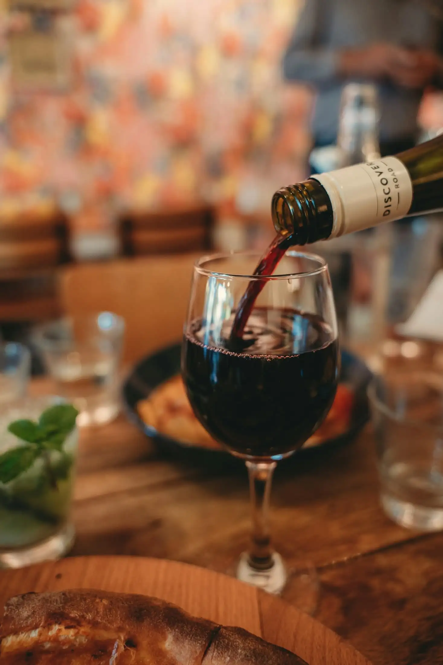 Red wine poured from a bottle into a glass on a restaurant table, in warm light.